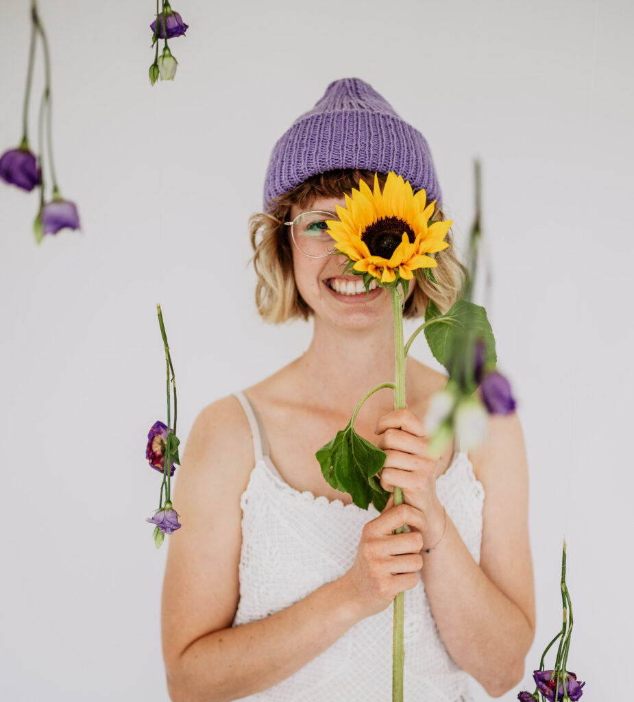 junge Frau vor weißer Wand mit Sonnenblume in der Hand